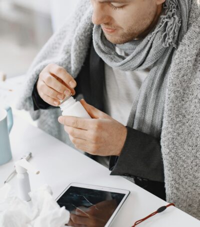 Man die aan een tafel zit met een deken om hem heen omdat hij verkouden is. Op tafel liggen allemaal snot doekjes