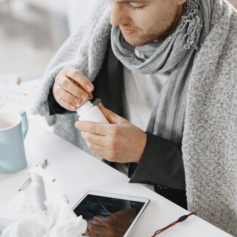 Man die aan een tafel zit met een deken om hem heen omdat hij verkouden is. Op tafel liggen allemaal snot doekjes
