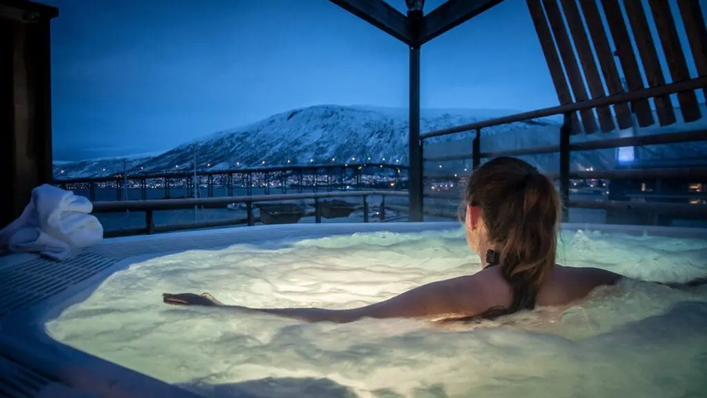Vrouw ontspant in een jacuzzi tijdens de winter, met een berglandschap op de achtergrond bij schemering