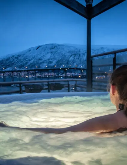 Vrouw ontspant in een jacuzzi tijdens de winter, met een berglandschap op de achtergrond bij schemering