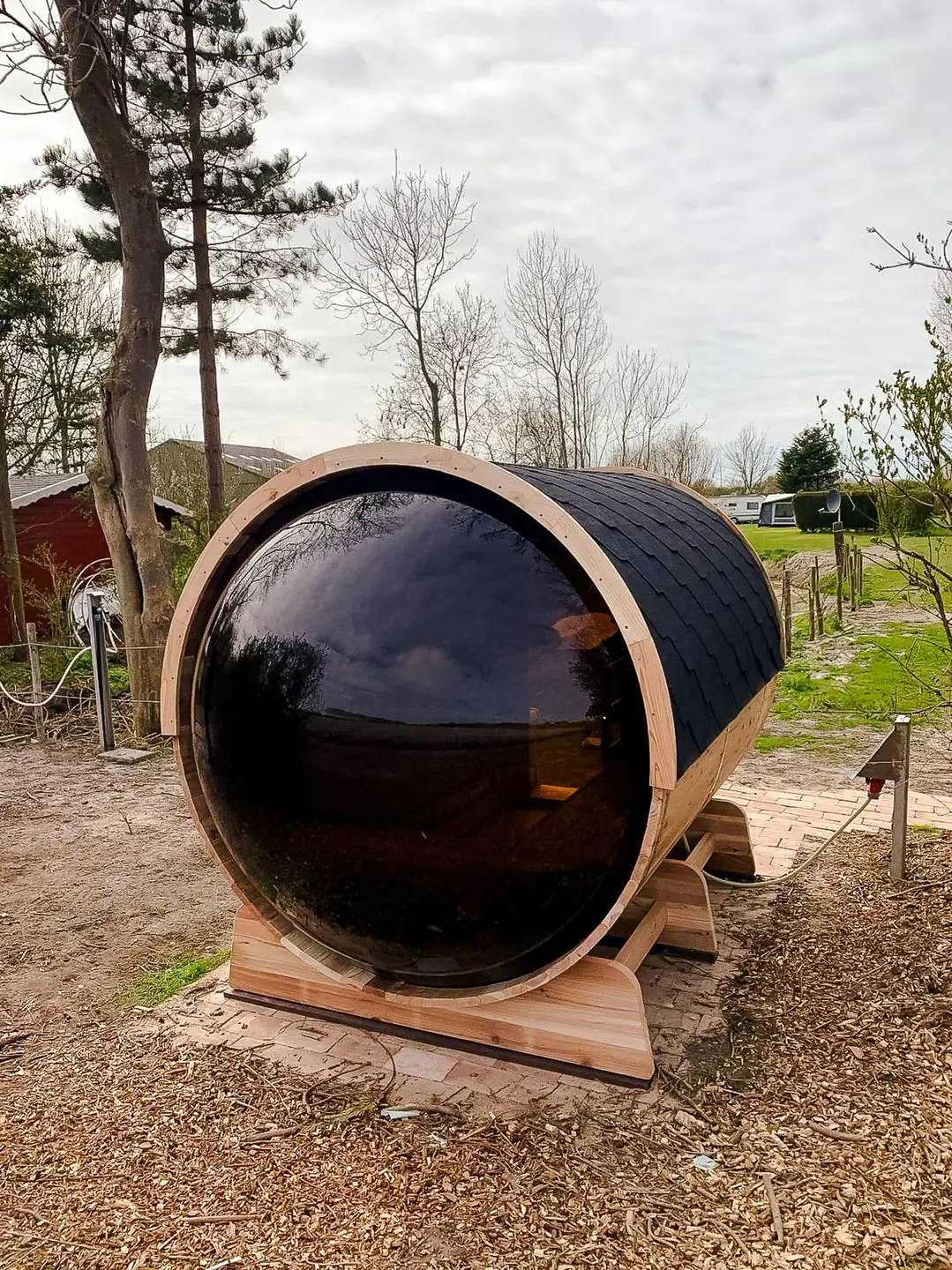 Buiten barrelsauna 230 van red cedar met bolle wanden en zwarte afwerkingen, geplaatst in de natuur tijdens de herfst