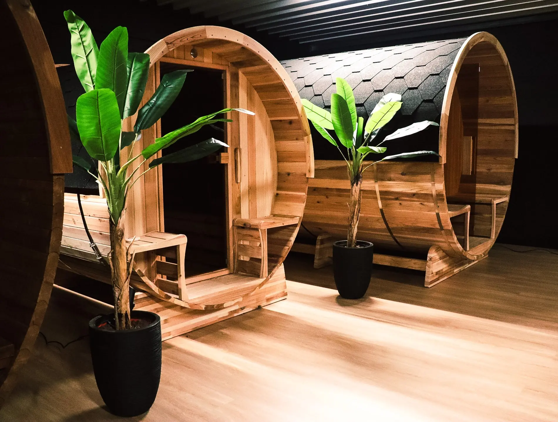 Twee houten barrelsauna’s in showroom met planten en houten vloer