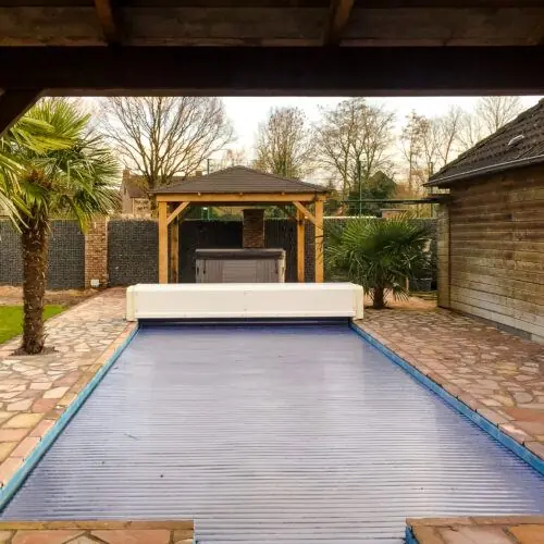Zwembad met mozaïektegels op de voorgrond en een jacuzzi spa onder een afdak van Wellnesshuis Benelux op de achtergrond