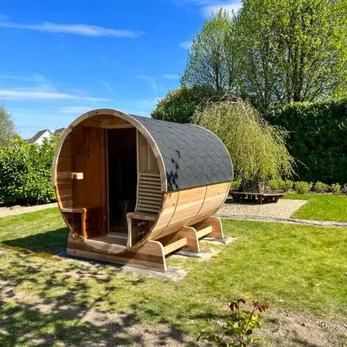 Barrelsauna in een tuin onder een heldere blauwe lucht