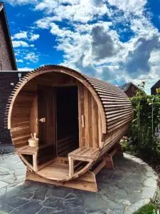Barrel sauna in een tuin met een blauwe lucht met wolken op de achtergrond