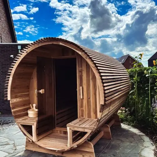 Barrel sauna in een tuin met een blauwe lucht met wolken op de achtergrond